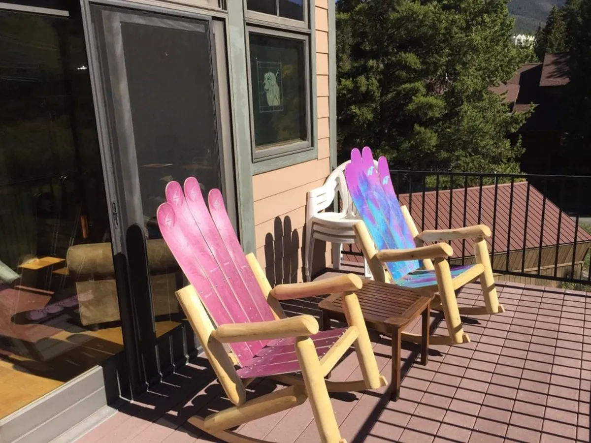 The scene shows a cheerful balcony with colorful chairs arranged along the railing, presenting a welcoming outdoor space that overlooks the surrounding natural landscape. The playful arrangement and open view invite guests to relax, sip coffee, or share a laugh with friends while reveling in the tranquility of nature.