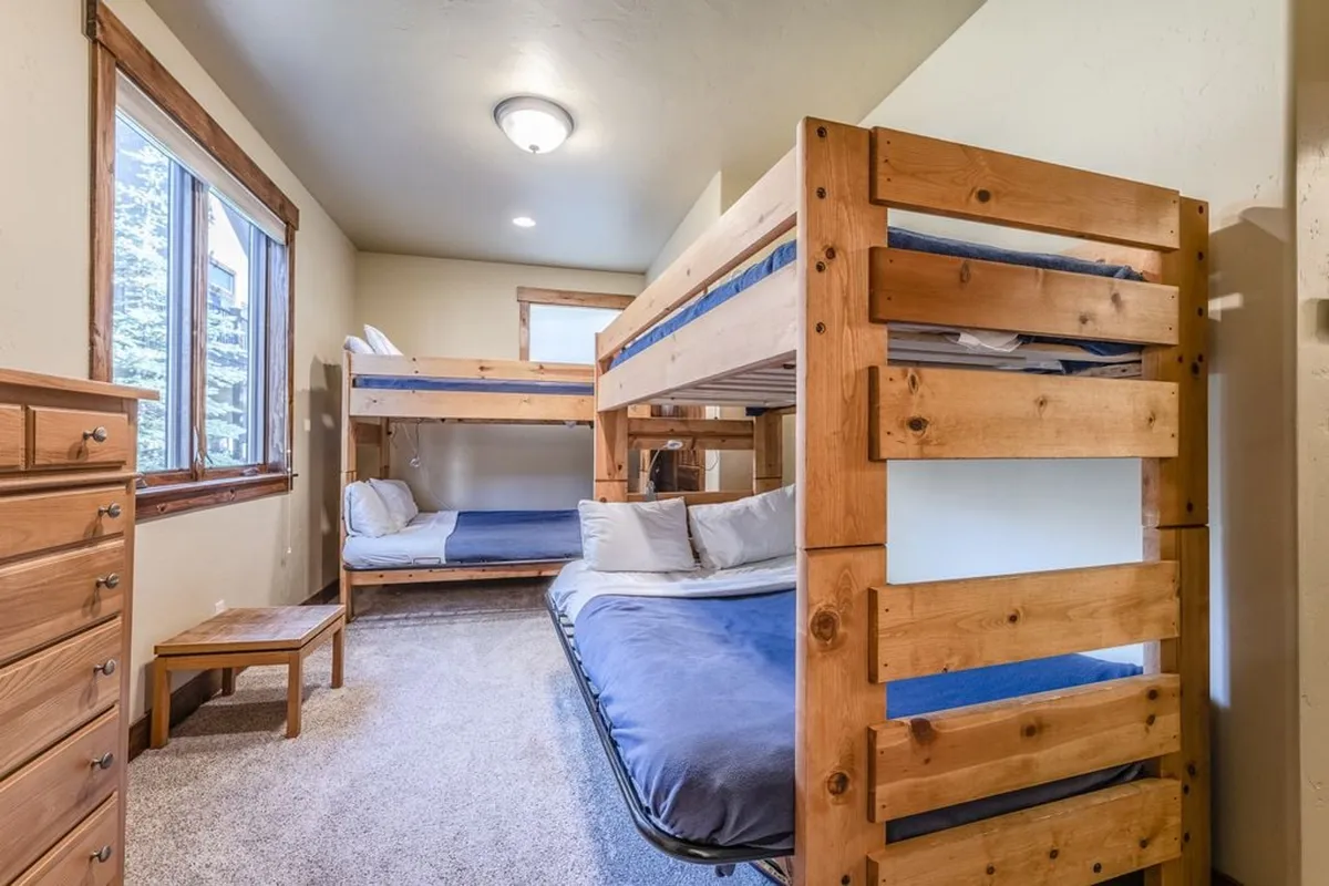 A cheerful and comfortable guest bedroom set up with bunk beds, a window bringing in natural light, and a wooden dresser. The playful arrangement of beds and inviting decor makes it ideal for families or groups, emphasizing flexible sleeping arrangements.