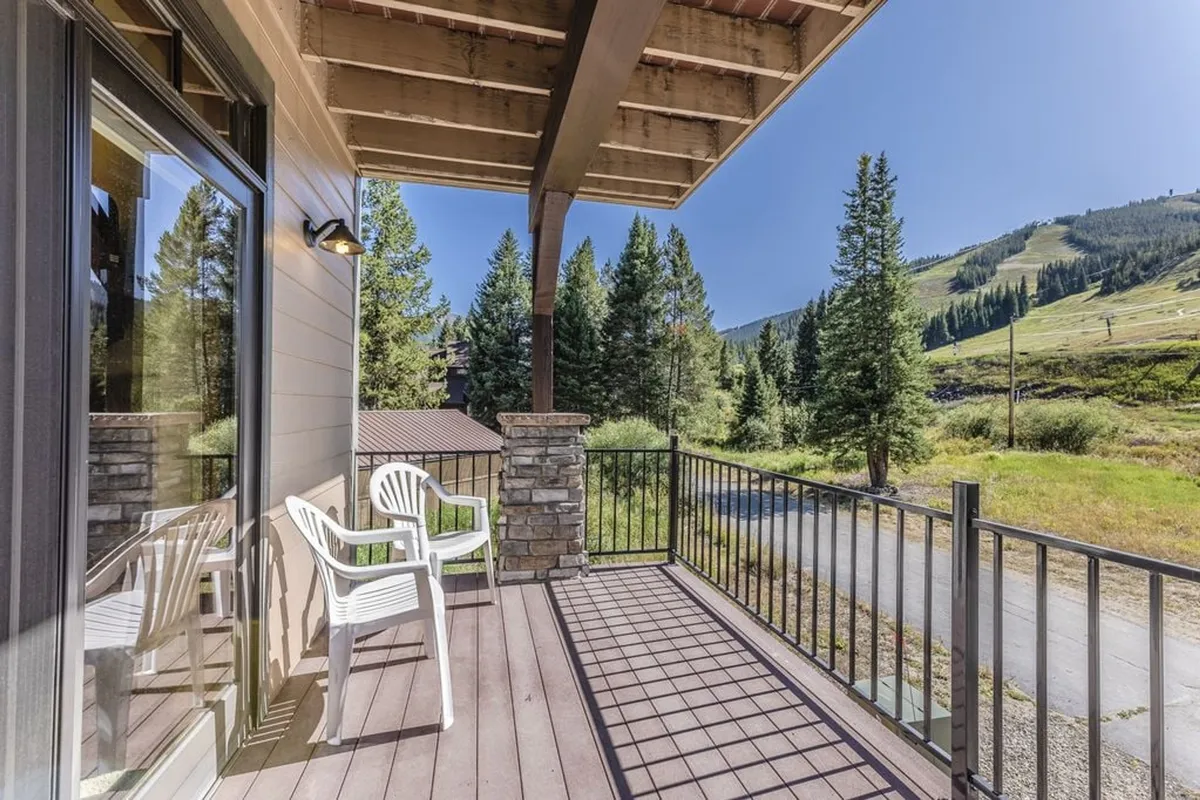 This image captures a serene balcony setting with comfortable chairs positioned beside a sturdy stone pillar, overlooking a sweeping mountain view. The soft light suggests early morning or late afternoon, enhancing the calm and inviting atmosphere—perfect for unwinding and enjoying the scenery after a day of adventure.