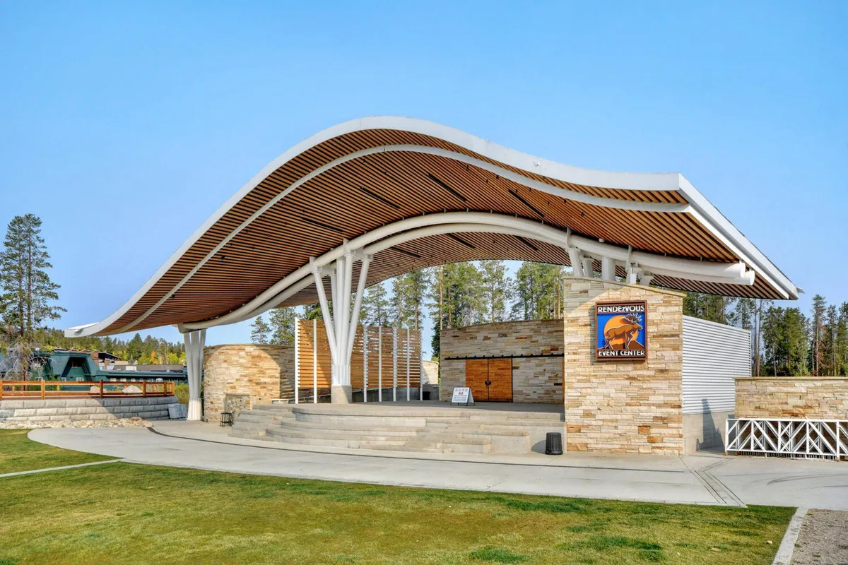 An open-air stage area with a curved roof structure and stone façade is set up for concerts and community events. People are gathered around, suggesting live music or a cultural event, with an energetic, welcoming mood that highlights social experiences.