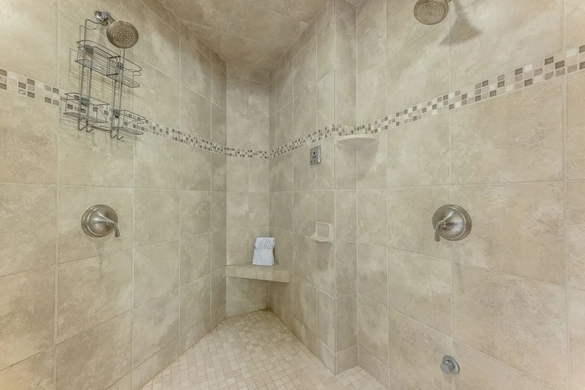 A close-up of a modern, spa-inspired shower with textured wall tiles, sleek fixtures, and a built-in bench. The inviting ambiance suggests relaxation and post-adventure rejuvenation, embodying the 'steam shower' feature described in the content.